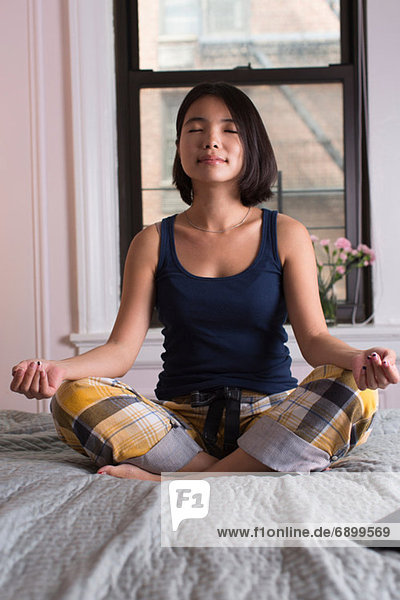 Junge Frau auf dem Bett sitzend und meditierend