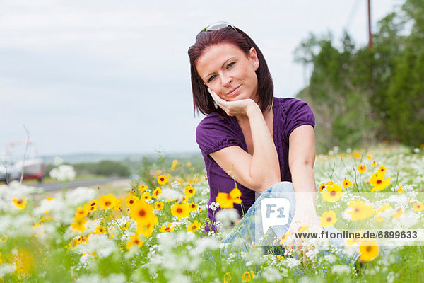 Mittlere erwachsene Frau auf einem Blumenfeld sitzend