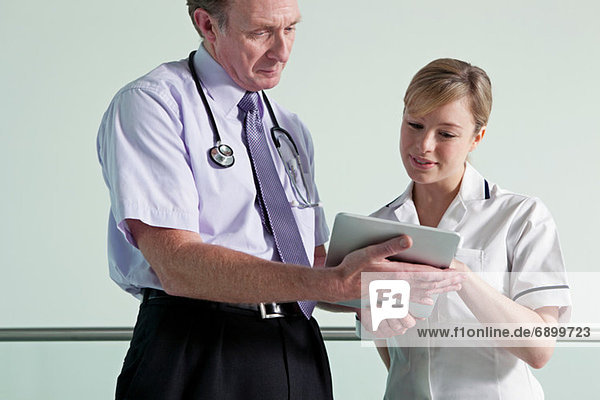 Arzt und Krankenschwester diskutieren über Krankenakten auf digitalem Tablett