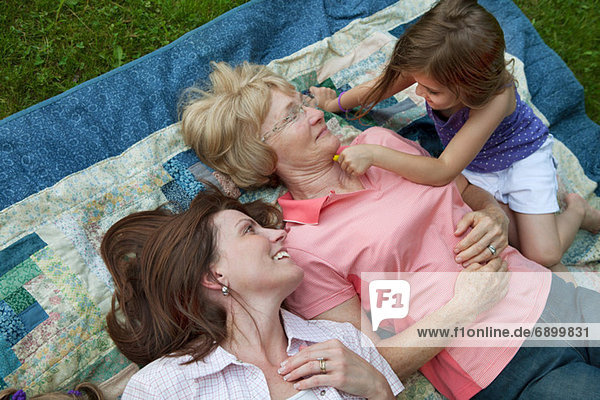 Drei Generationen Familie auf Picknickdecke liegend