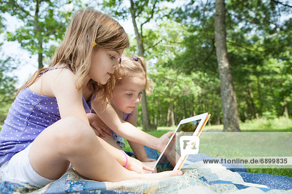 Two girls sitting on picnic blanket with digital tablet