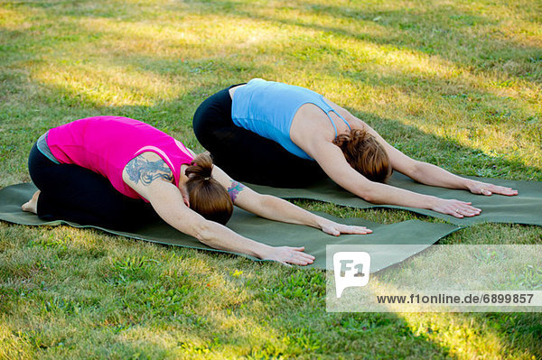 Zwei Frauen  die sich auf Yogamatten im Freien ausstrecken.