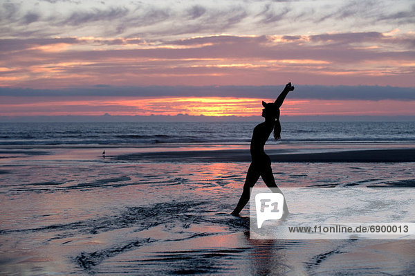 Silhouette of young woman stretching by the sea at sunset