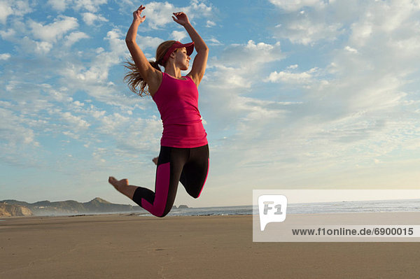 Junge Frau beim Springen in der Luft am Strand