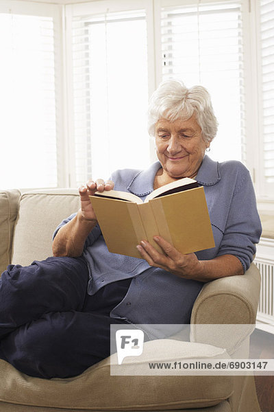 Senior Woman Sitting on Sofa Reading Book