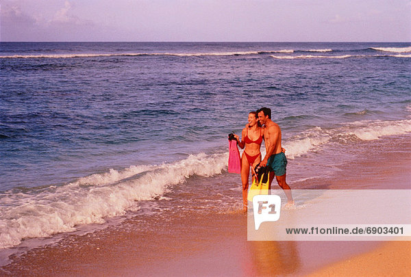 Couple in Swimwear  Walking on Beach Holding Flippers