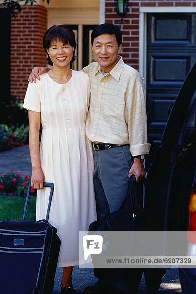 Portrait of Mature Couple in Front of House with Luggage