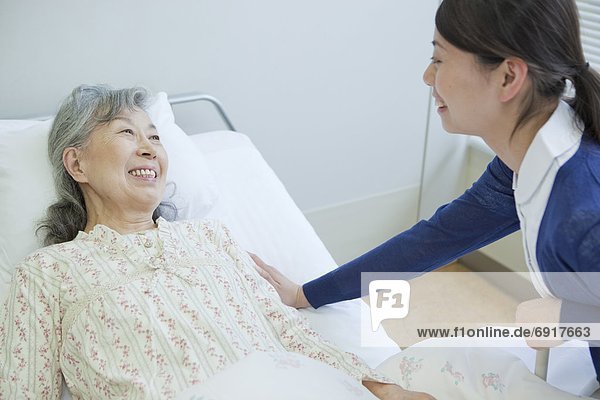 Senior woman lying on bed talking to nurse  Kanagawa Prefecture  Honshu  Japan