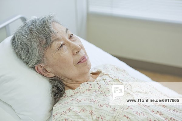 Senior woman lying on bed  Kanagawa Prefecture  Honshu  Japan