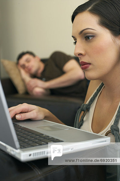 Woman Working at Computer and Man Napping on Couch