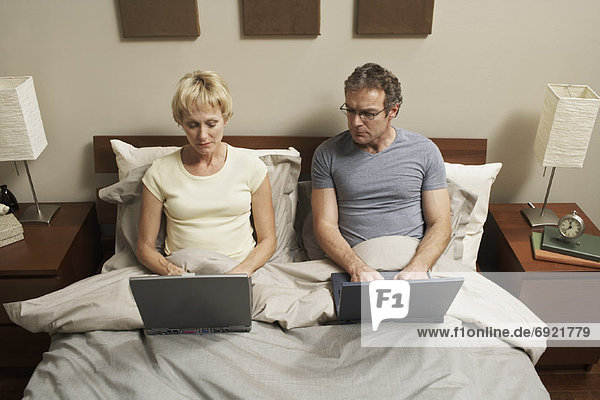 Paar mit Laptops im Bett