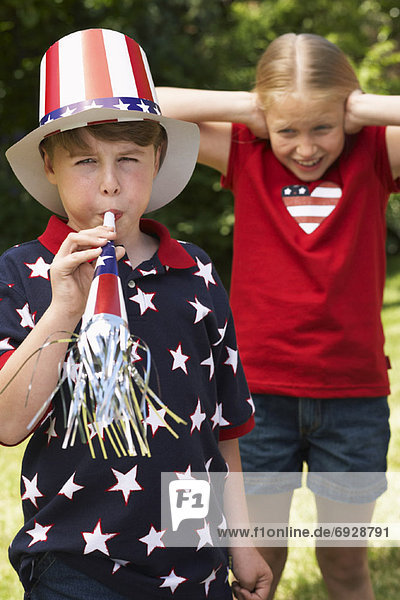 Portrait of Boy Wearing Stars and Stripes Top and Hat  Blowing Noisemaker Horn  Girl Watching