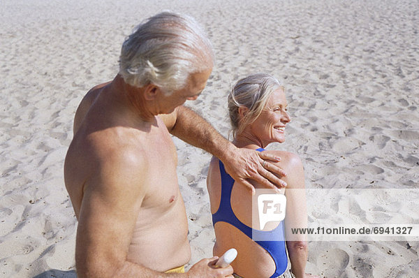 eincremen verteilen Mann Sonnencreme Frau auftragen Paar am Strand