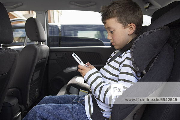 Boy Playing Hand Held Game  Sitting in Back Seat of Car