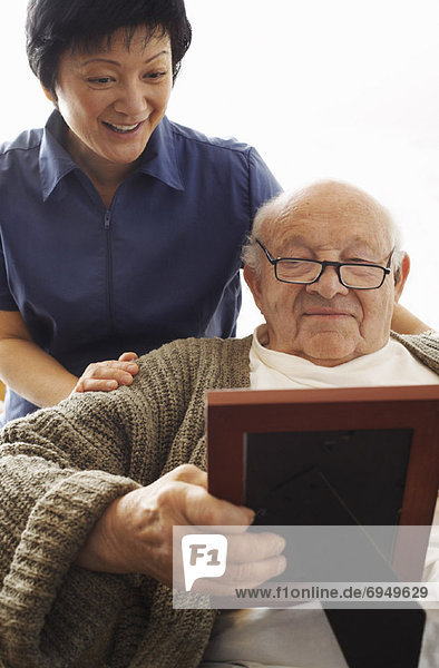 Senior Man Looking at Picture with Woman Looking over his Shoulder