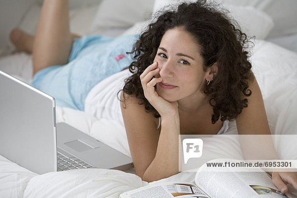 Woman with Laptop and Magazine on Bed