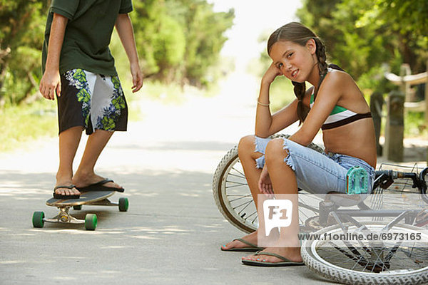 Little Girl Sitting on Bike  Boy Skateboarding