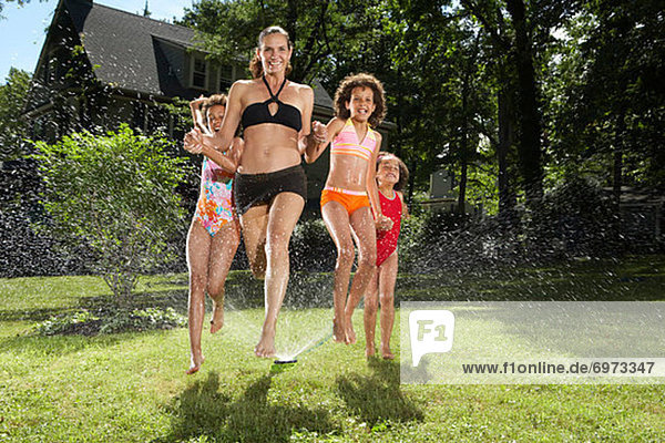 Mother and Children Playing in Backyard with Sprinkler