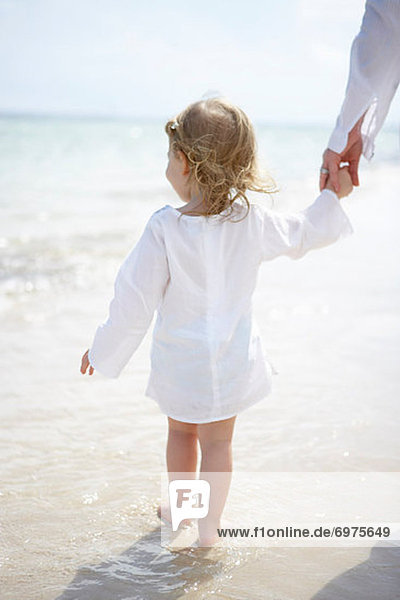 Backview of Little Girl Holding Mothers Hand and Walking on Beach