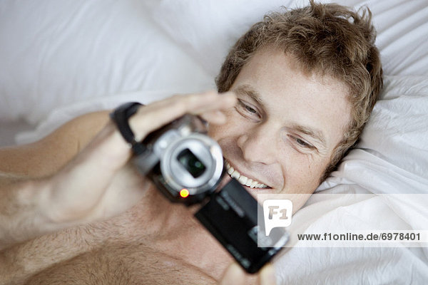Man Lying in Bed Holding a Video Camera
