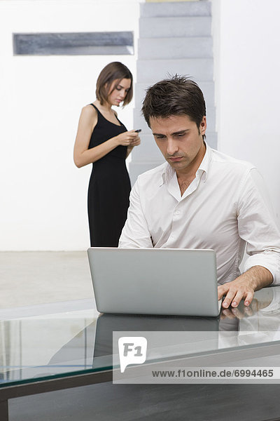 Businessman Using Laptop Computer  Businesswoman in the Background With Cell Phone