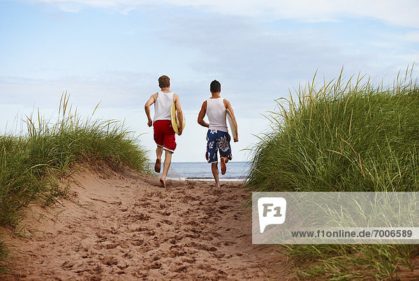 Young Men holding Skimboards while Running to Beach  PEI  Canada