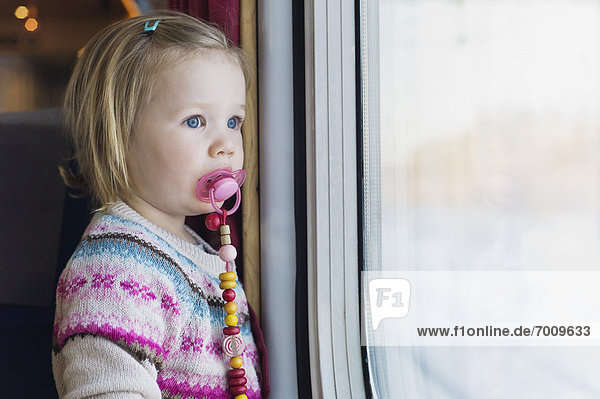 Portrait of Little Girl using Pacifier and Looking out Train Window