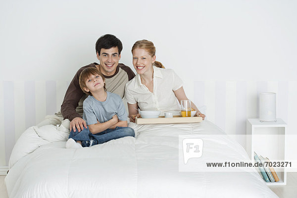 Young family sitting in bed  mother holding breakfast tray