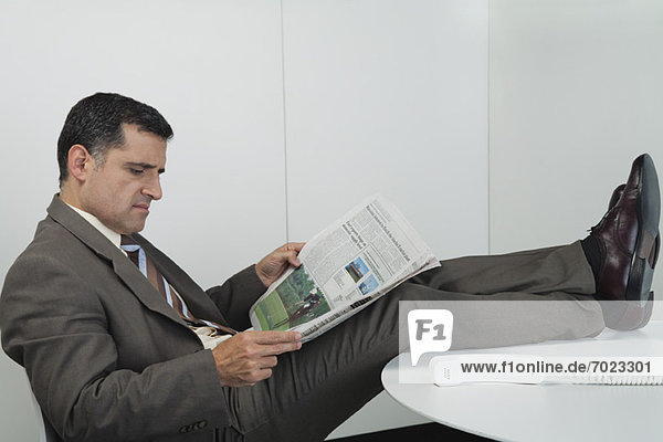 Businessman reading newspaper in office with feet up on desk