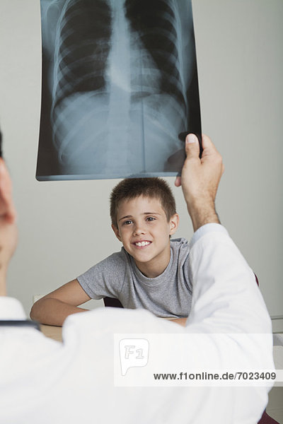 Junge lächelt  während der Arzt auf das Röntgenbild schaut