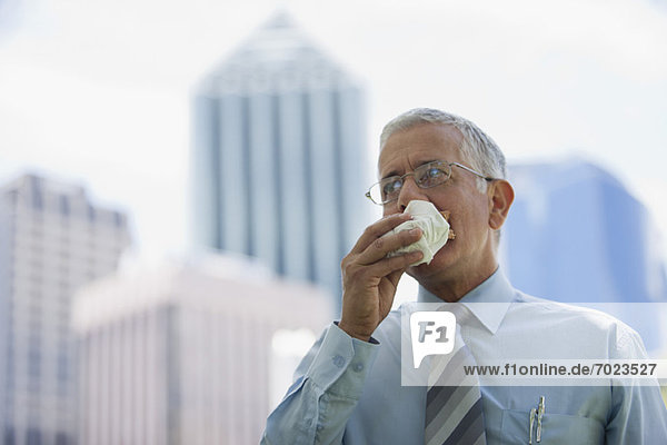 Mature businessman eating lunch while walking outdoors