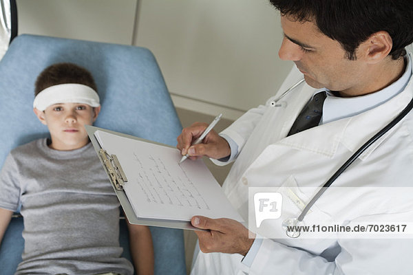 Arzt überwacht jungen Patienten mit Verband am Kopf