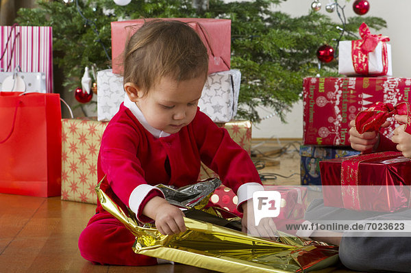 Baby Mädchen beim Auspacken des Weihnachtsgeschenks