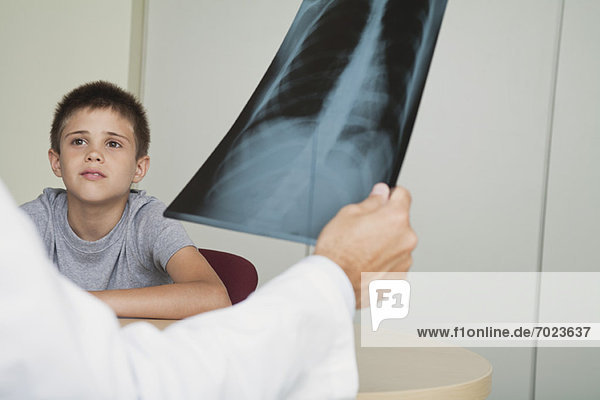 Arzt sitzt dem Jungen gegenüber und schaut auf das Röntgenbild.