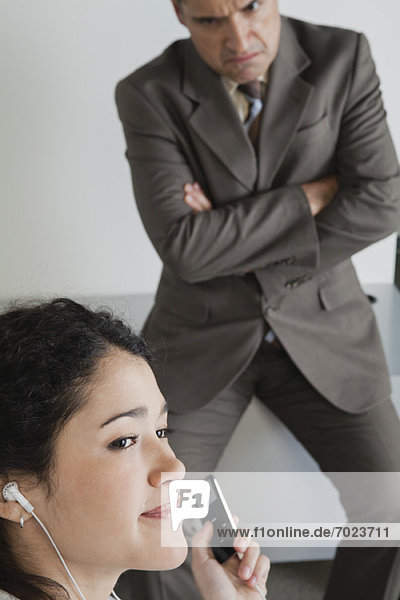 Frau hört bei der Arbeit abgelenkt MP3-Player  wütender Chef im Hintergrund