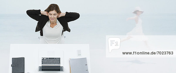 Reife Geschäftsfrau sitzt am Schreibtisch und stellt sich am Strand vor.