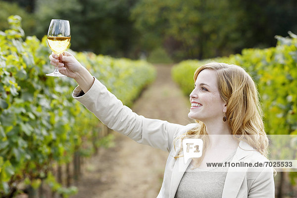 Young woman holding glass of white wine in vineyard