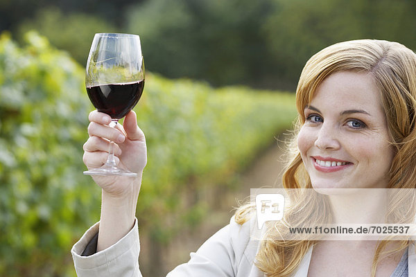 Young woman holding glass of red wine in vineyard (portrait)