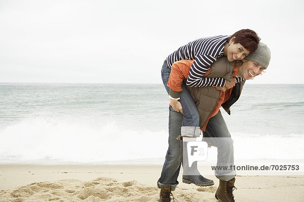 Giving Frau Mann piggyback am Strand