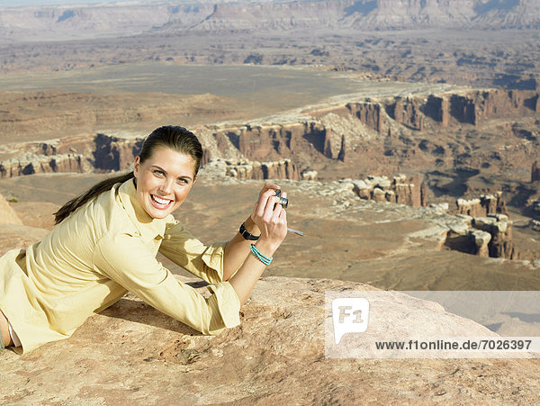 Young woman lying on cliff and photographing rock strata