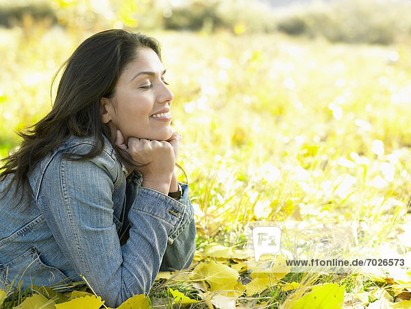 Mid adult woman lying on autumn leaves and day dreaming