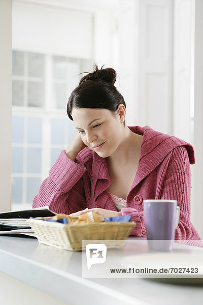 Mid adult woman reading magazine at kitchen counter