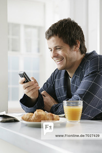 Mid adult man using cell phone at breakfast table
