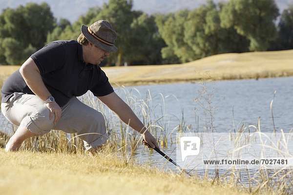 Man looking for golf ball in pond