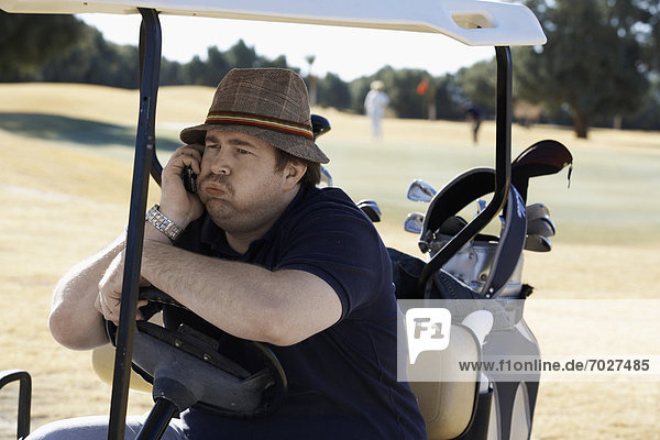Bored man talking on phone in golf cart