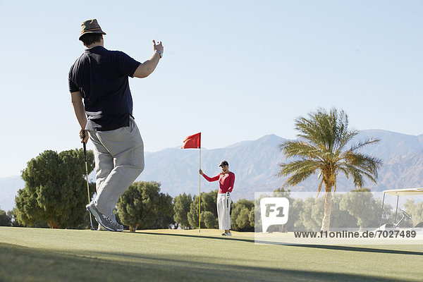 Man playing golf  woman holding golf flag
