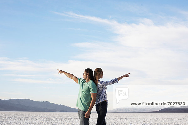 Couple standing back to back and pointing to opposite directions by lake
