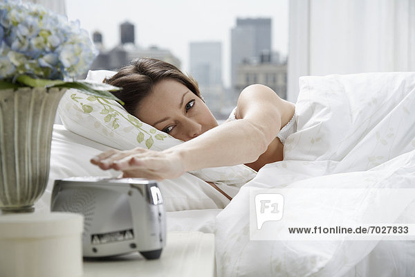 Mid adult woman reaching for alarm clock