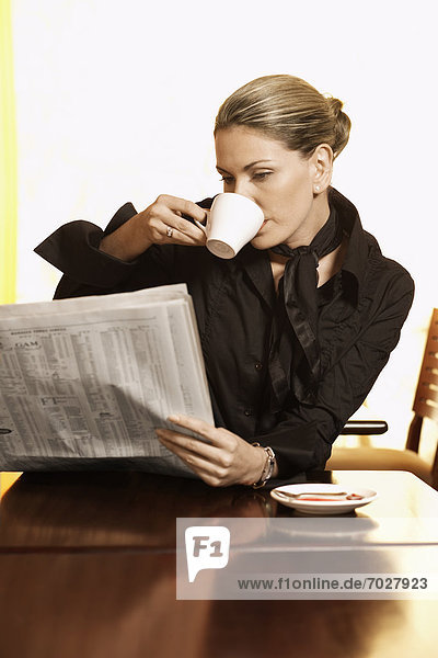 Mid adult woman drinking coffee and reading newspaper