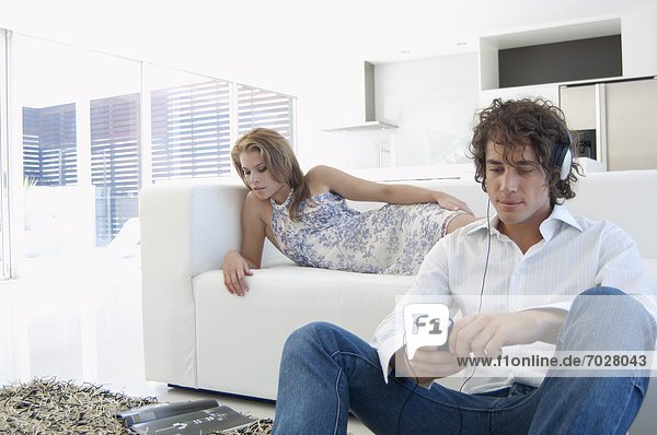 Young man listening to MP3 player  woman reading magazine on sofa